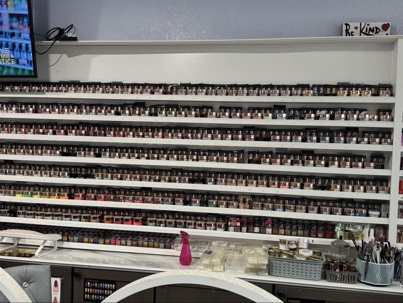 Dip powder wall at Euro Nail Lounge — shelves of dip powder jars by the Be Kind sign