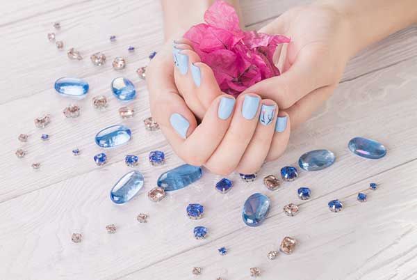 Manicure at Euro Nail Lounge — light blue polished nails holding a pink flower, surrounded by blue gems