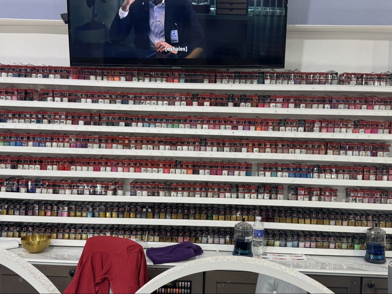 Dip powder wall at Euro Nail Lounge — shelves of dip powder jars beneath the salon TV